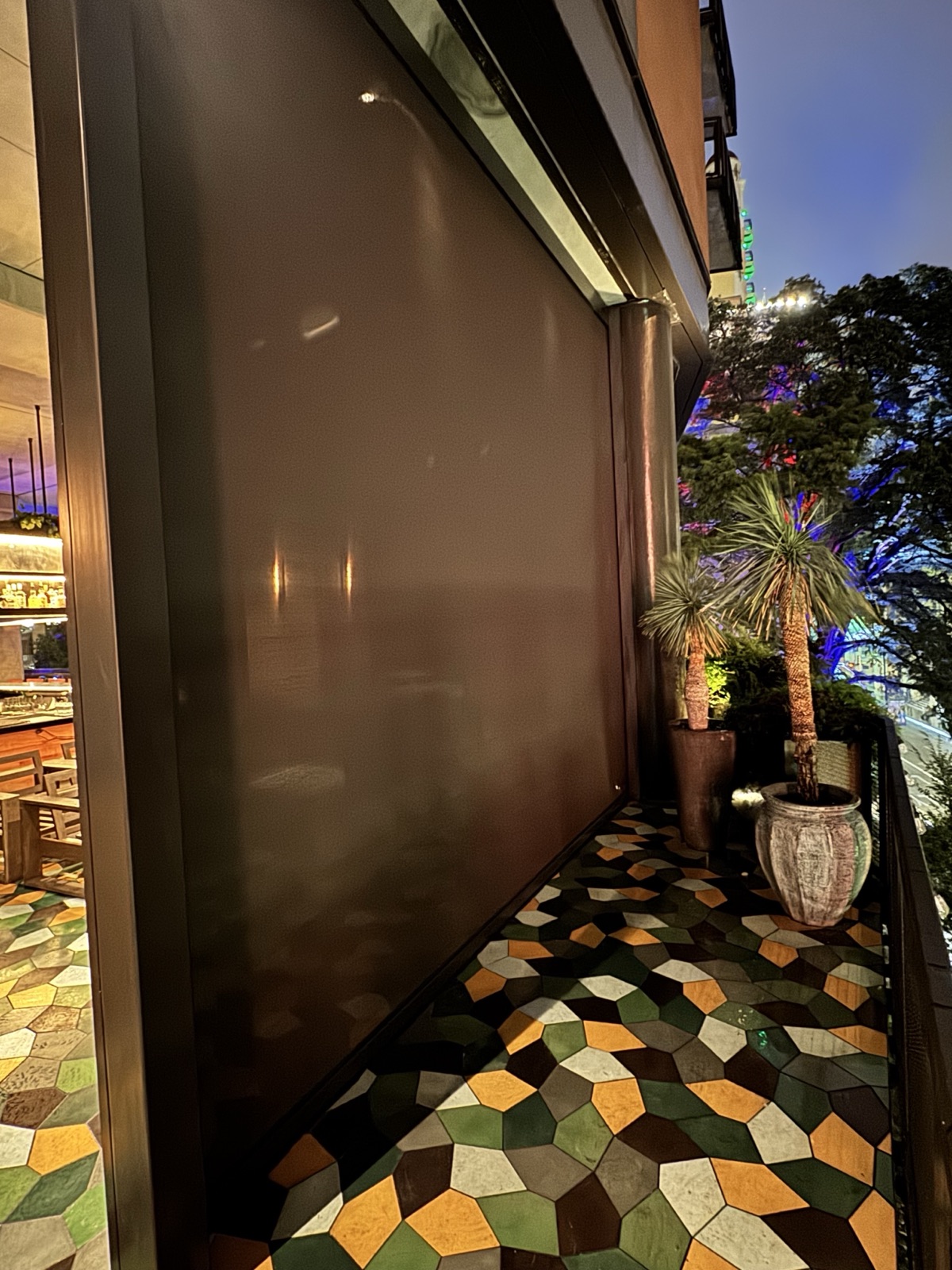 A tobacco Nano mesh curtain lowered on the rooftop patio, bronze side track against the concrete column