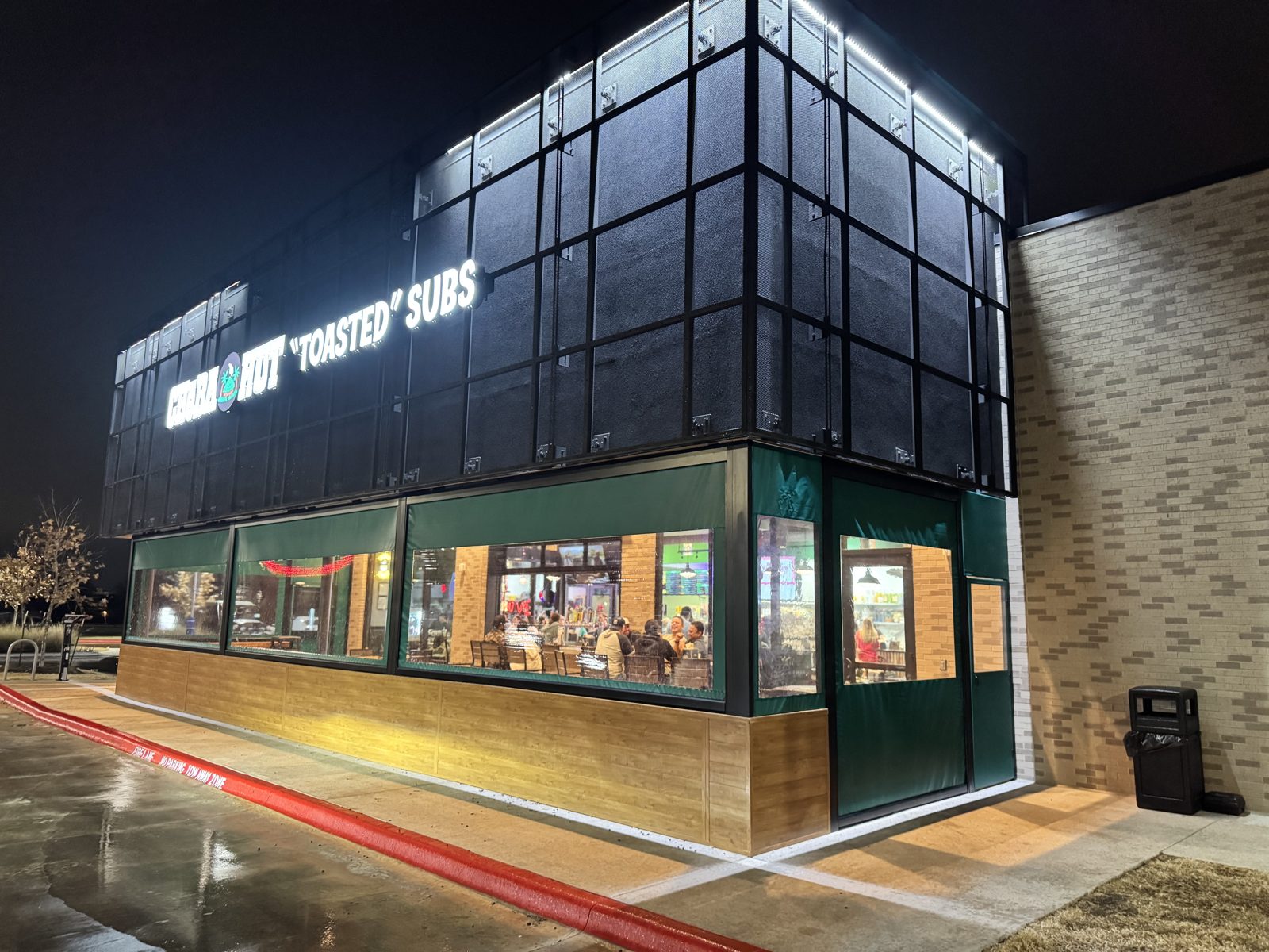 Cheba Hut South Austin at night: green motorized curtains with clear windows wrapping the patio under the black mesh tower
