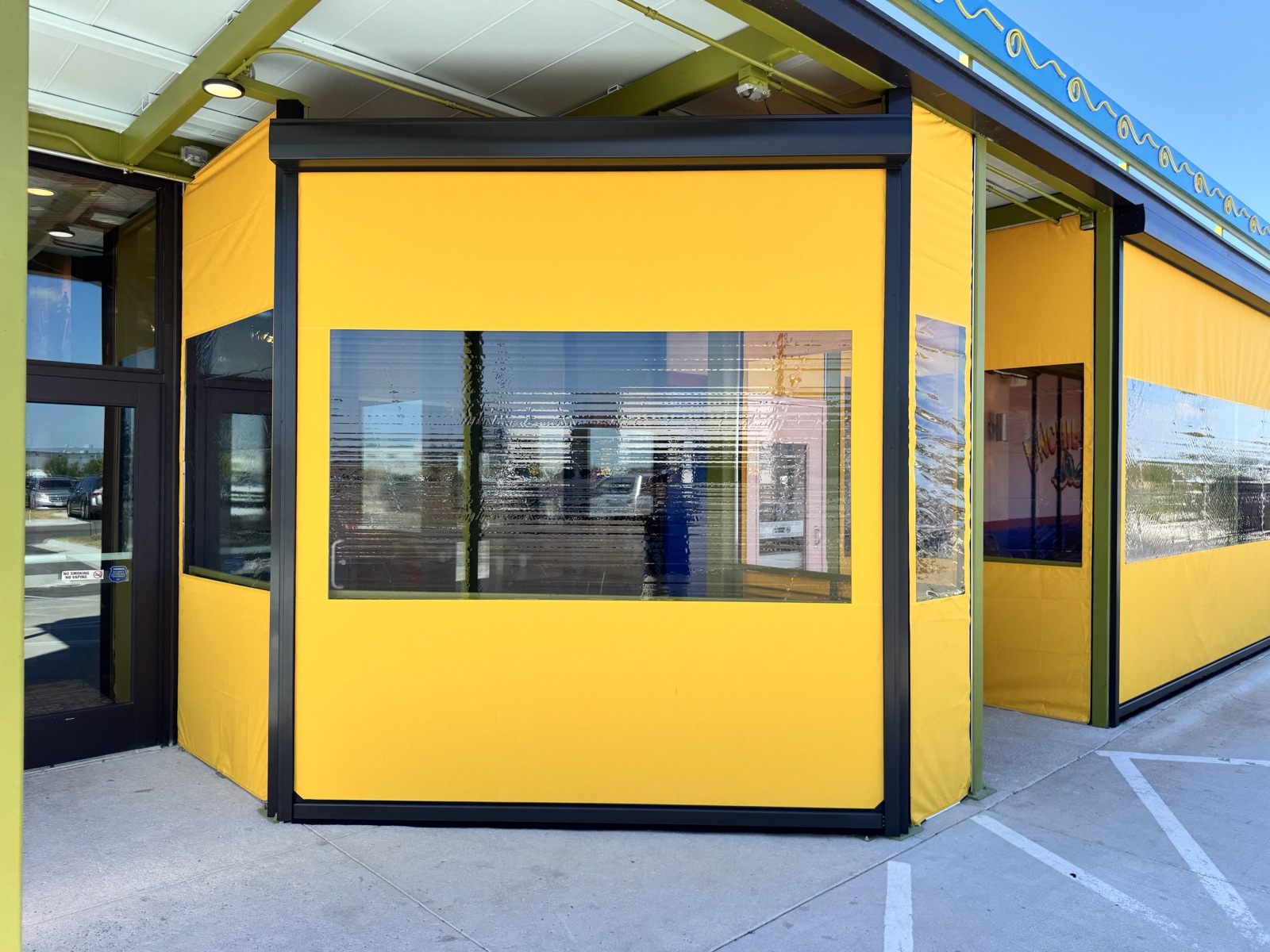 A clear-window curtain wrapping the corner of the Chuy's Manor patio, Seattle Yellow border, bronze track