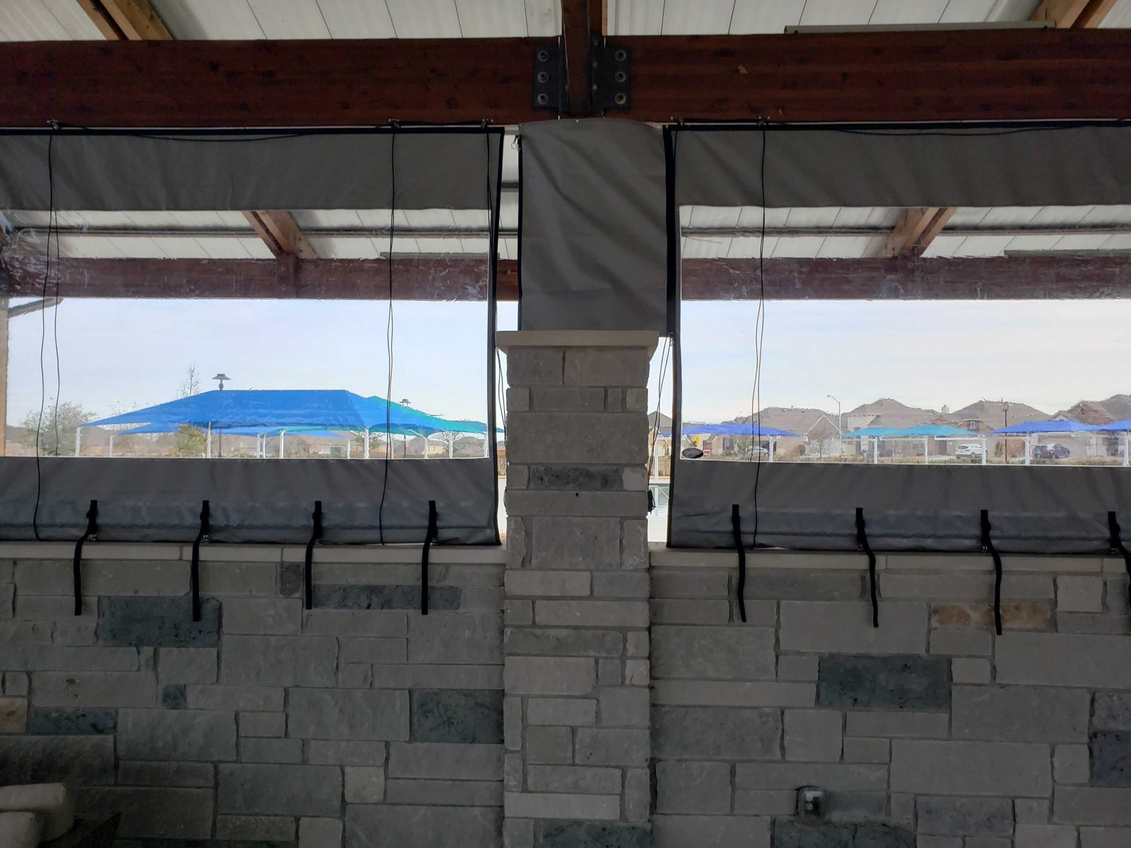 Two clear bays over the stone pony wall, the tie-downs cinched, the pool shade sails through the vinyl