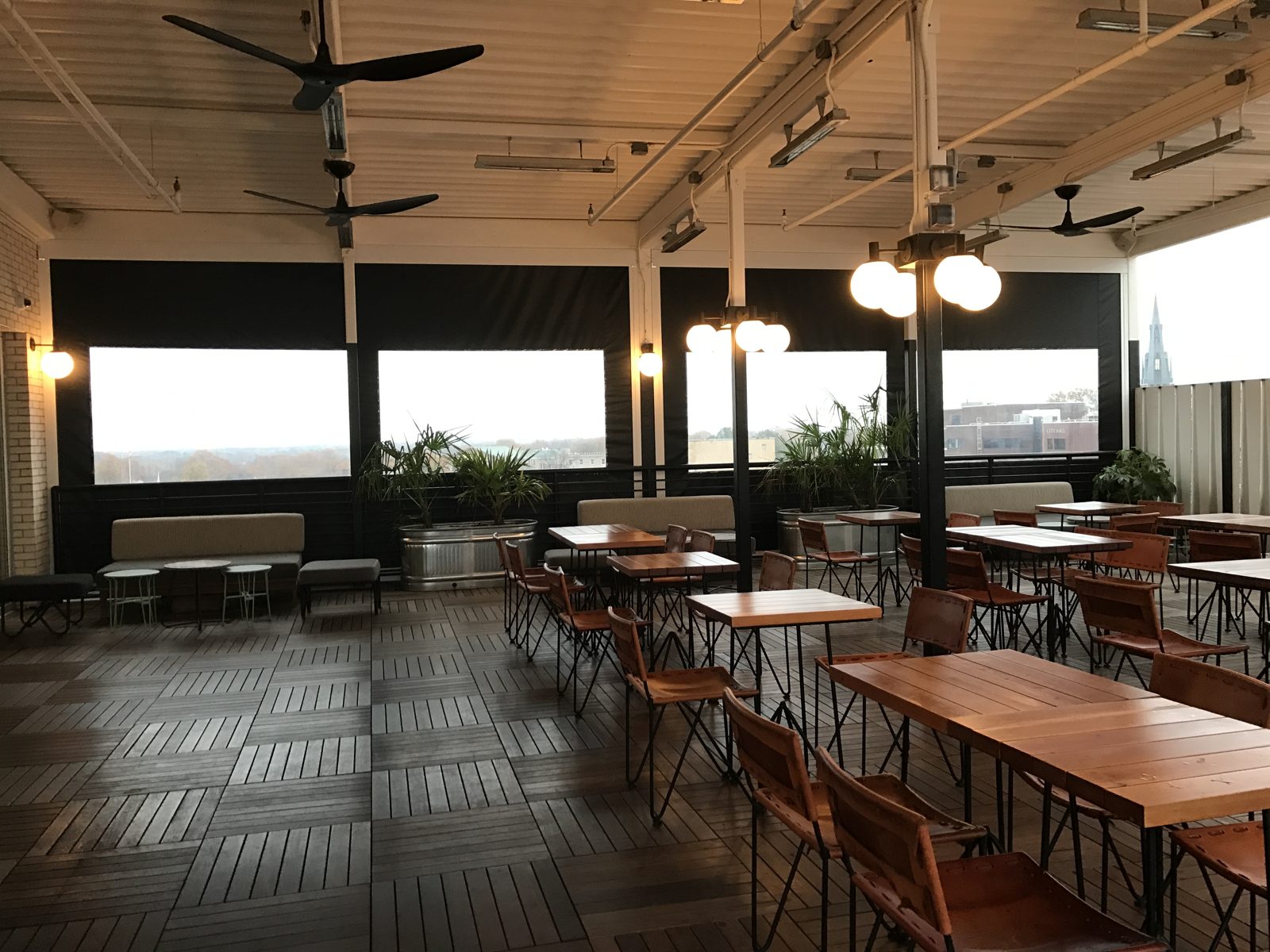 The Durham Hotel rooftop at dawn: black motorized screens half down over the rail, tables and globe lights under the slat roof