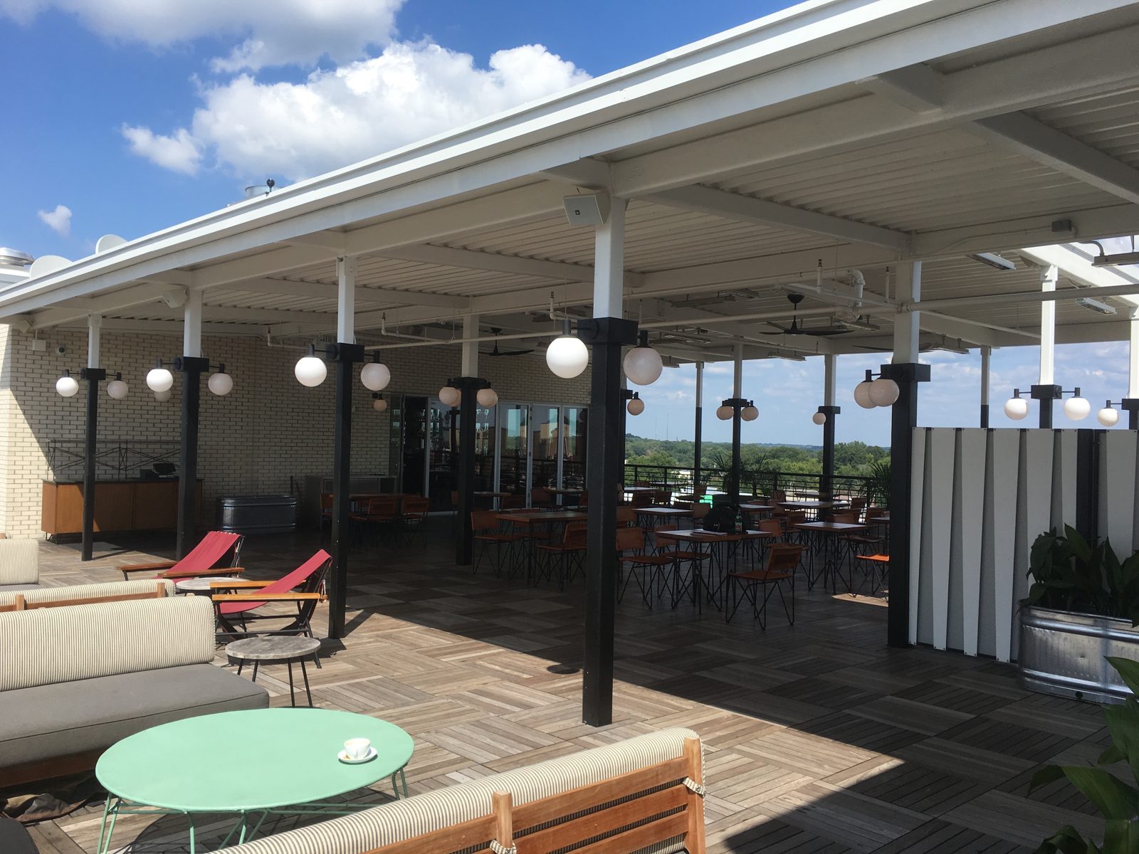 Before: the open rooftop in summer 2016, globe lights and lounge seating under the canopy, nothing at the rail