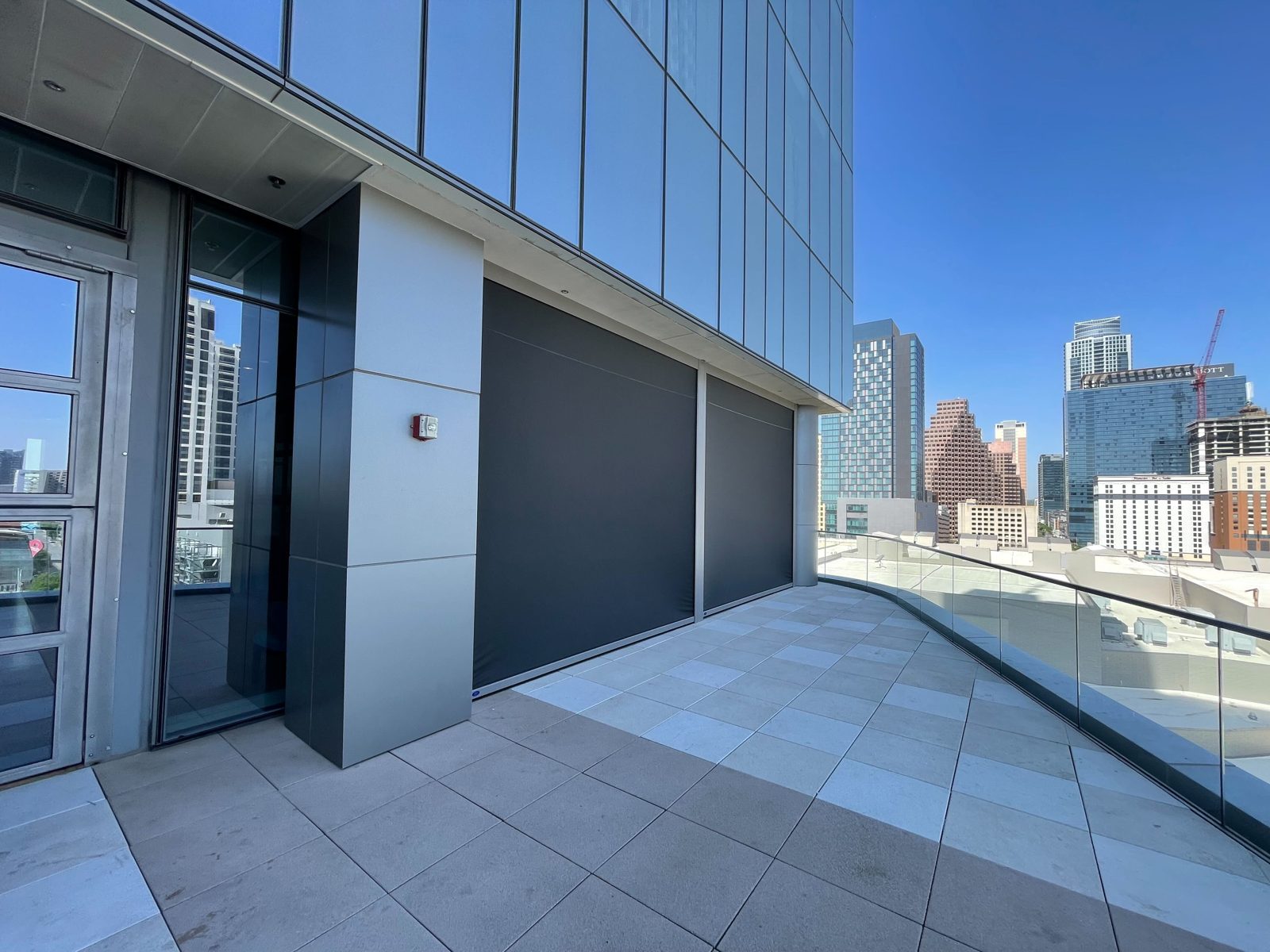 Two black motorized shades down on the curved terrace, the glass tower above and the Austin skyline beyond