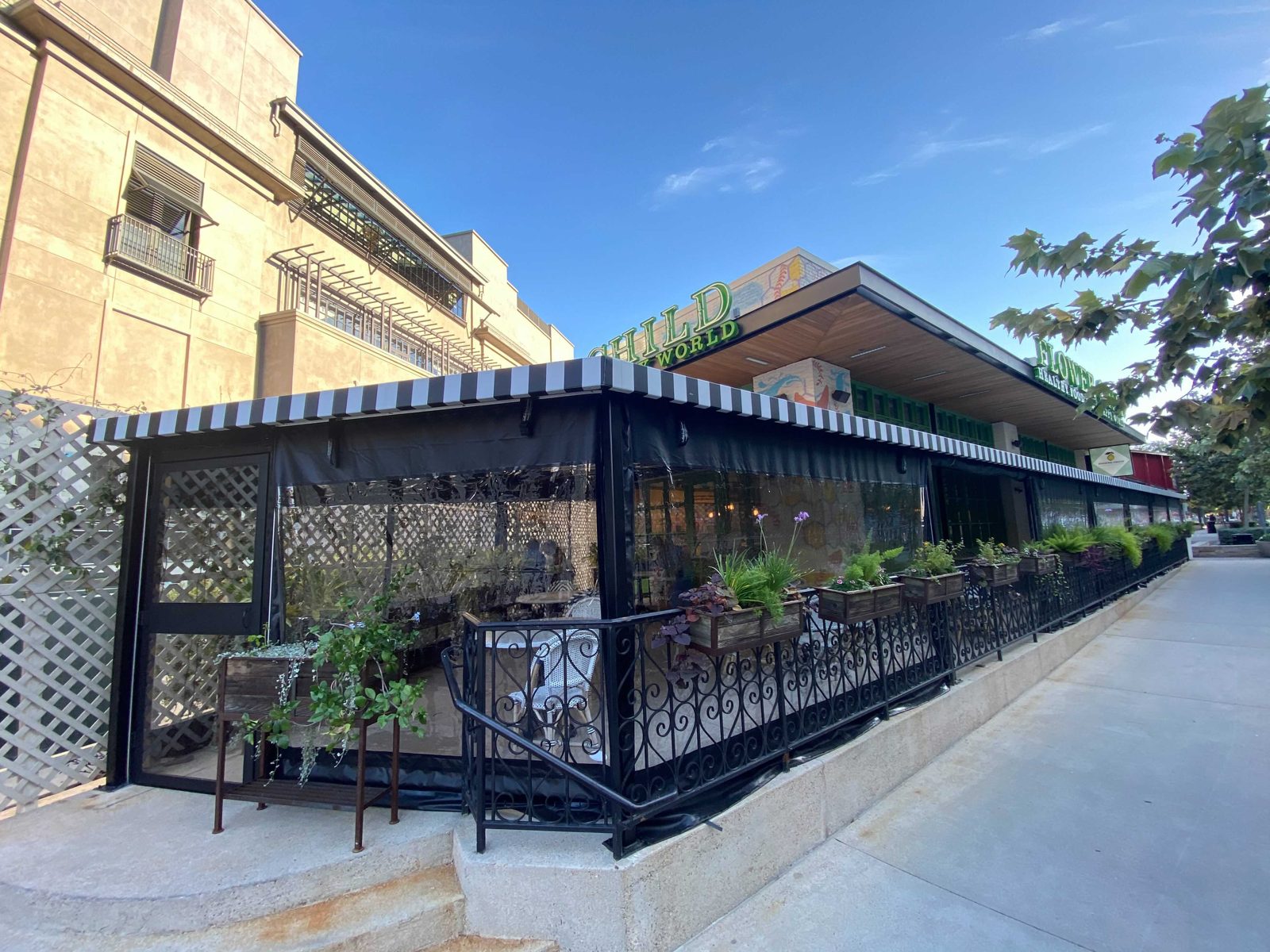 Flower Child at The Domain: black-bordered clear panels around the corner patio under the striped awning at dusk