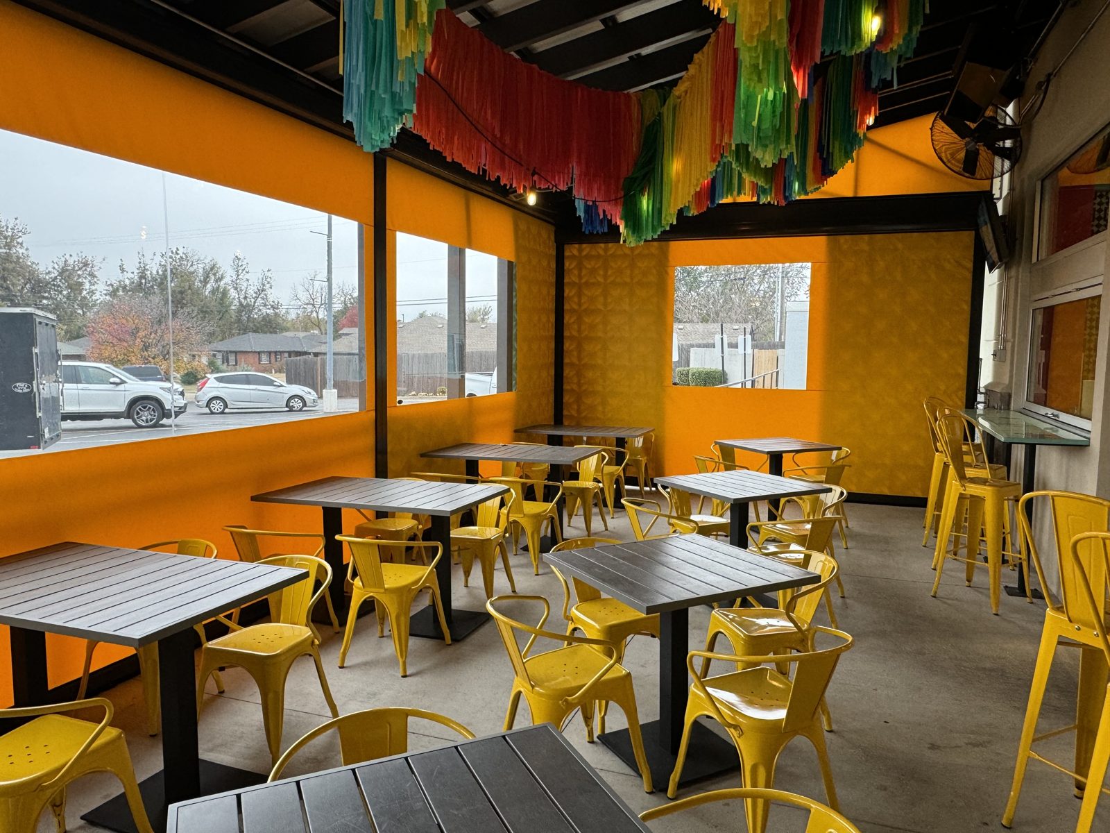 Inside Fuzzy's Oklahoma City: the yellow curtains closed with the clear window at the tables, the papel picado overhead