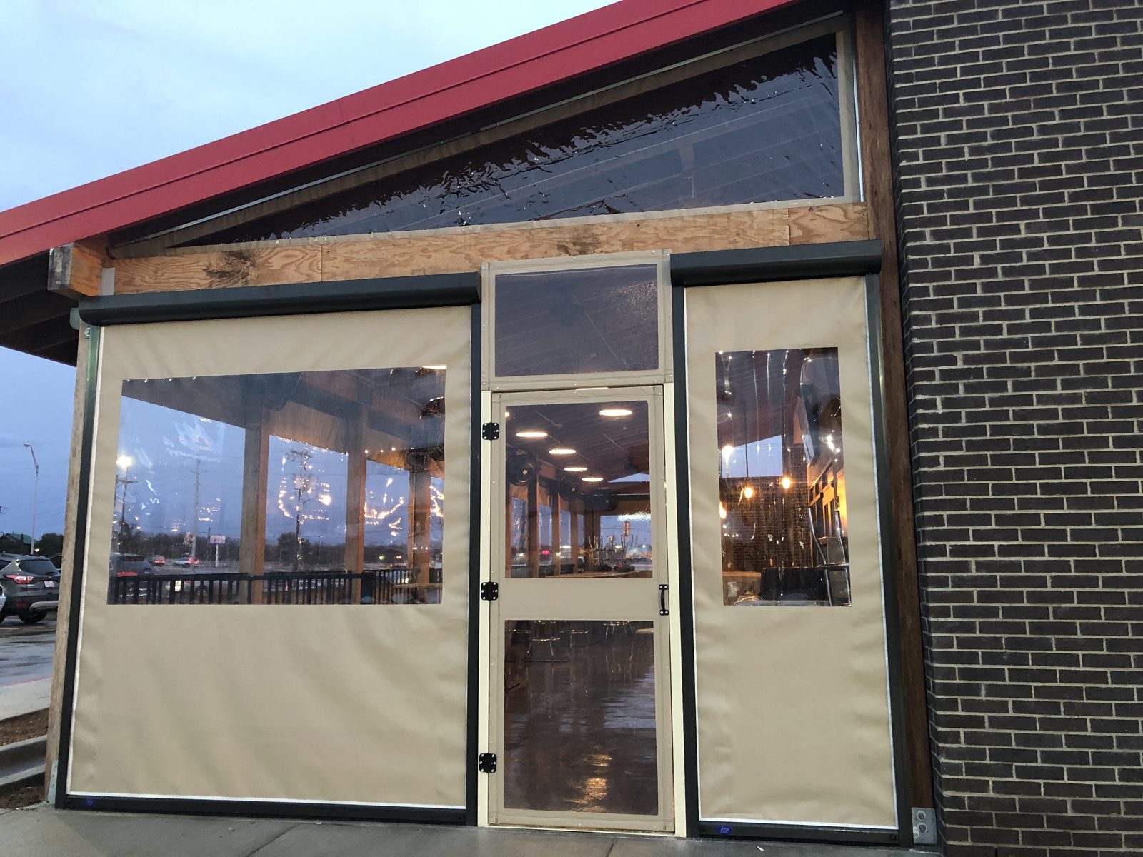 Fuzzy's Lake Worth: a tan motorized curtain with its clear window beside the framed door and transom under the red gable
