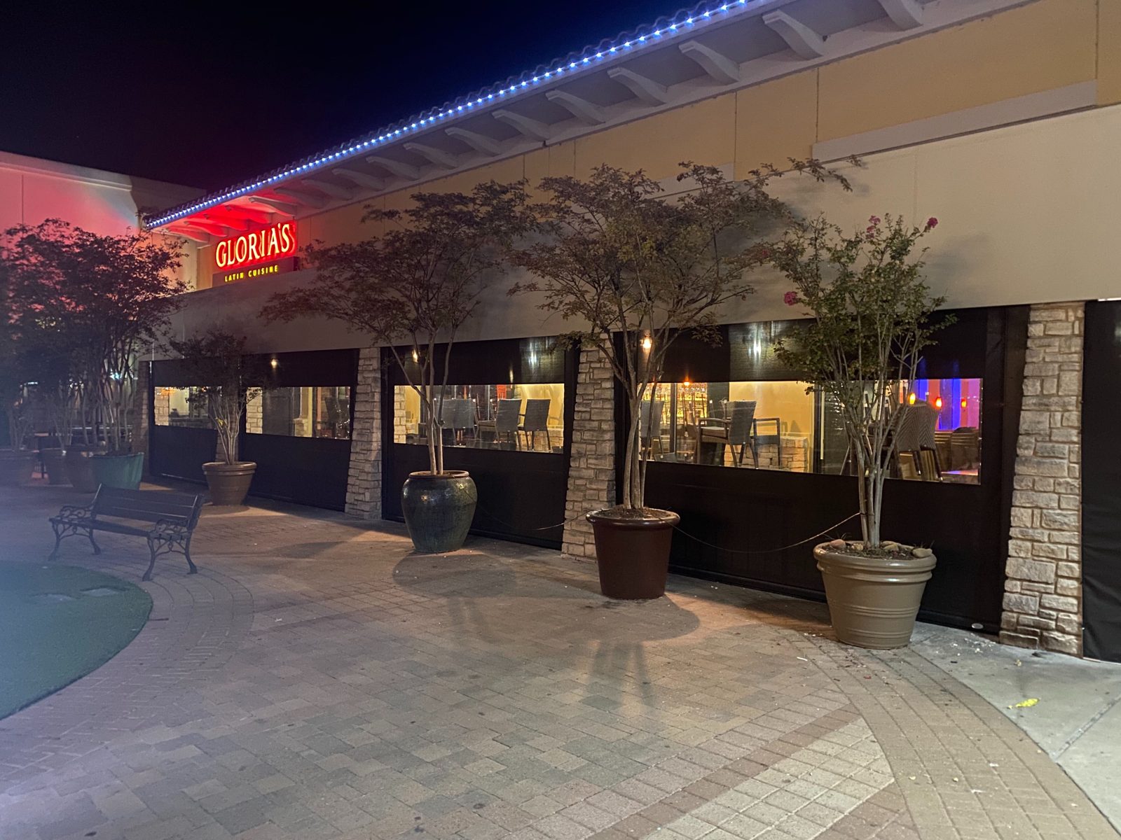 Gloria's Rockwall, the 2020 patio at night: screens down behind the trees and planters, the sign lit above