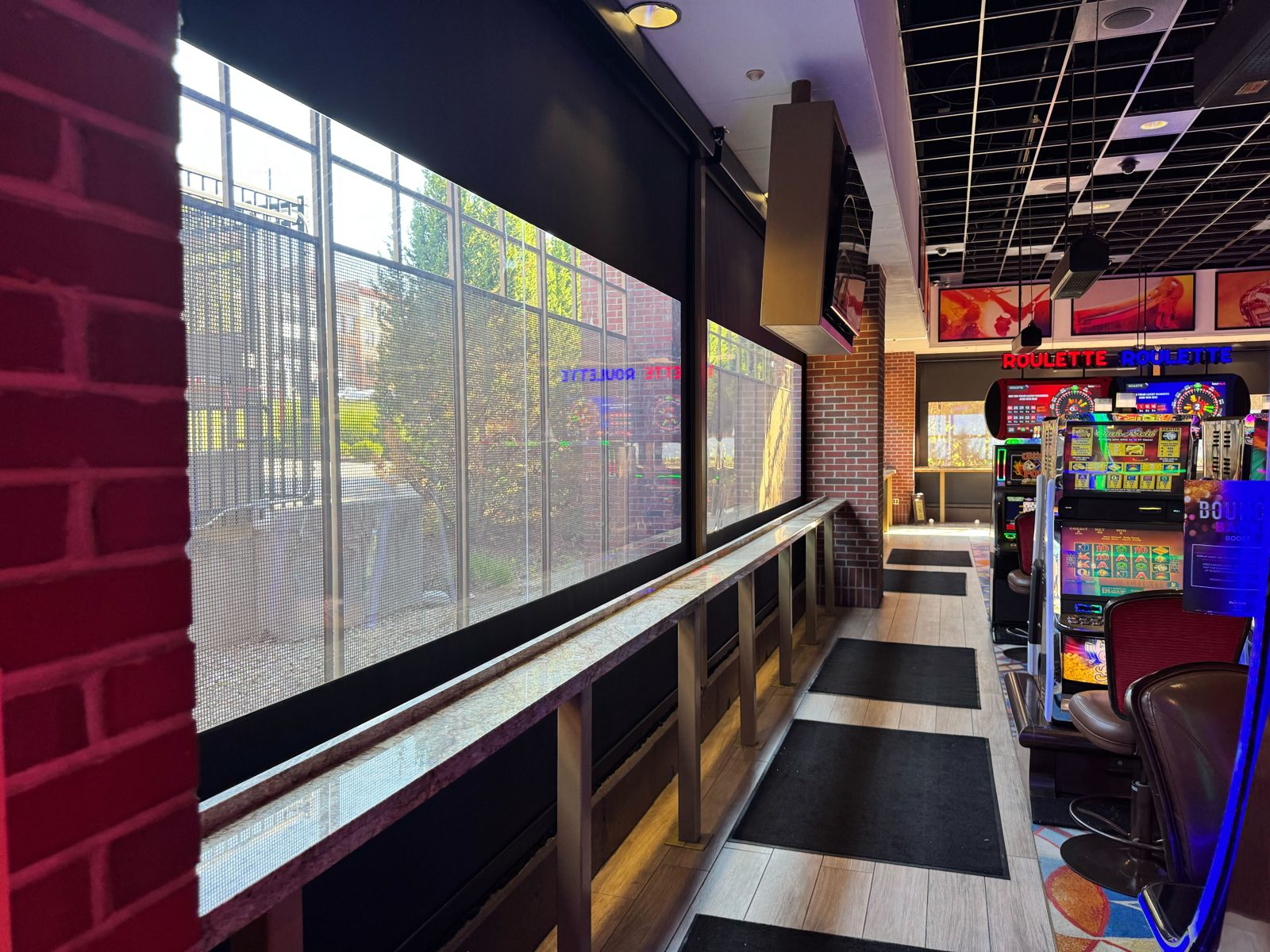 The West gaming patio: two shades down over the bar rail with the city behind the mesh