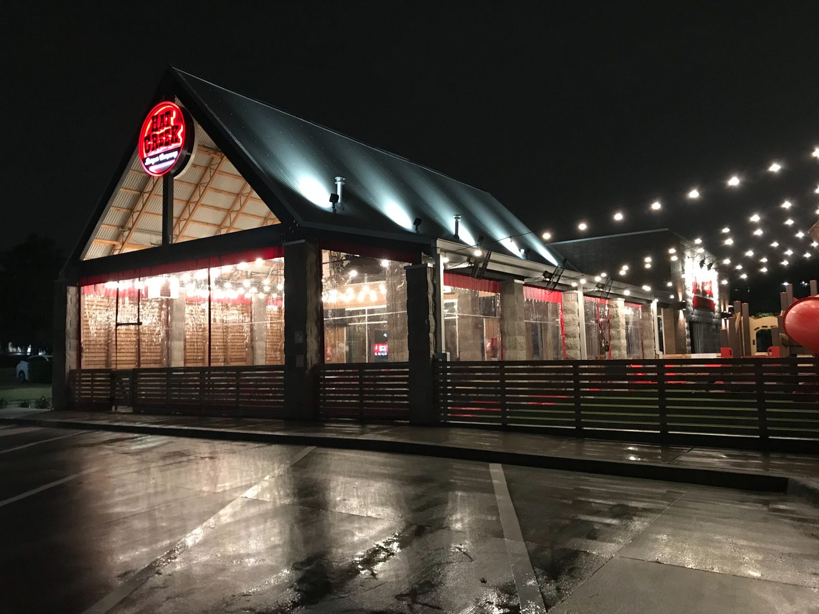 Hat Creek Richardson at night in the rain: the gable patio glowing through the clear panels, red borders under the eave