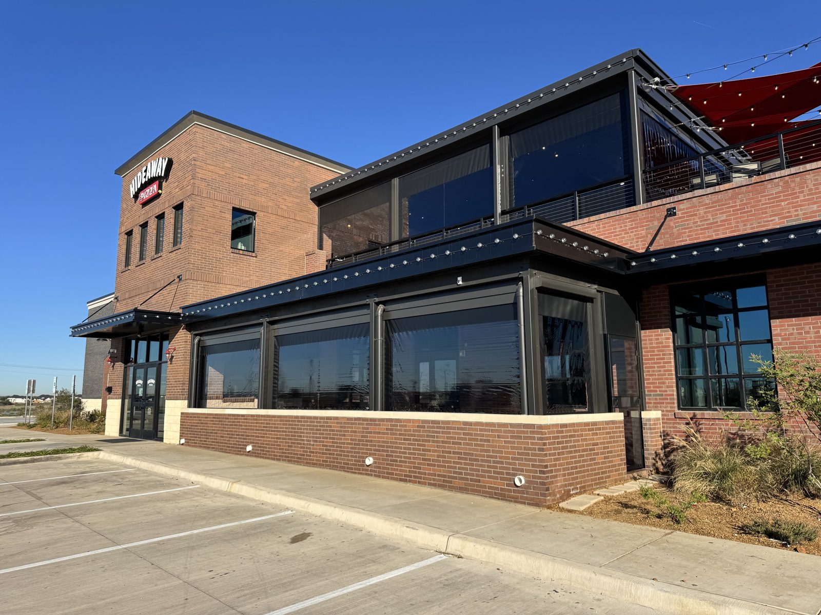 Hideaway Pizza McKinney: motorized screens on both the ground-floor patio and the rooftop terrace of the new brick building