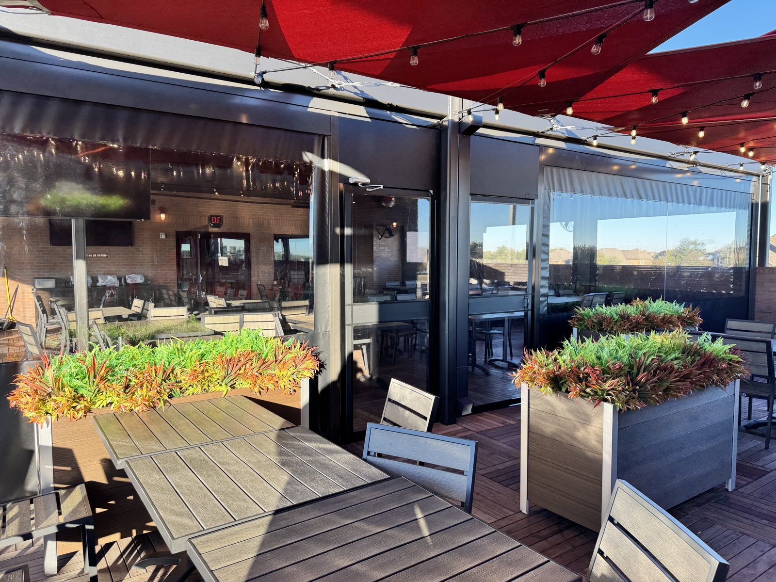 Inside the McKinney rooftop terrace: the red sails overhead, planters along the rail and the clear screens closed behind them