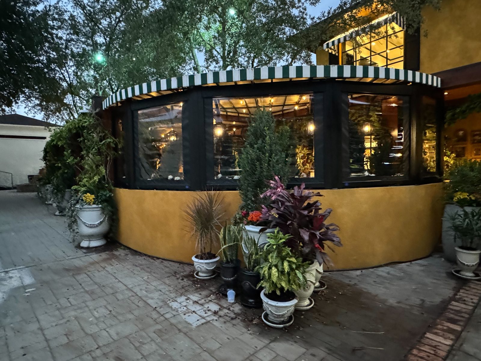 La Griglia Houston at dusk: five motorized clear screens following the curved yellow wall under the green and white awning