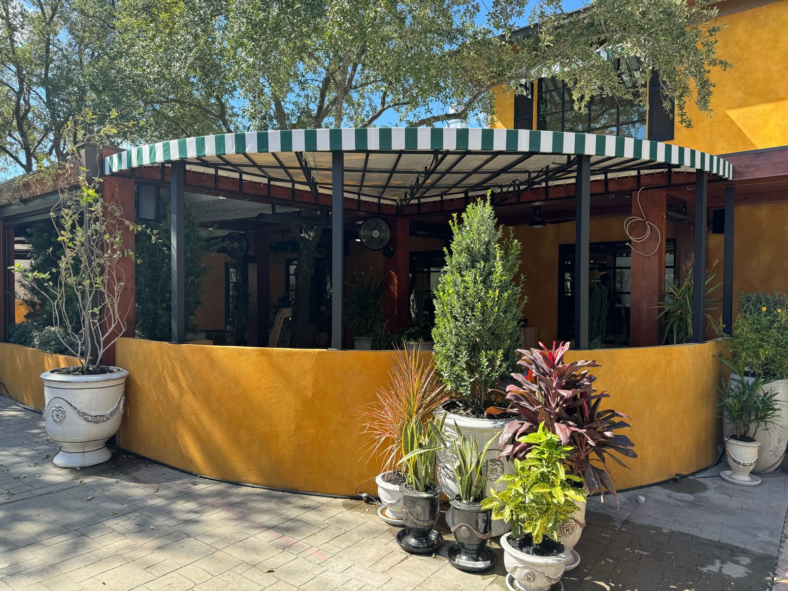 Before: the curved patio wall open under the awning in October 2023, planters along the base