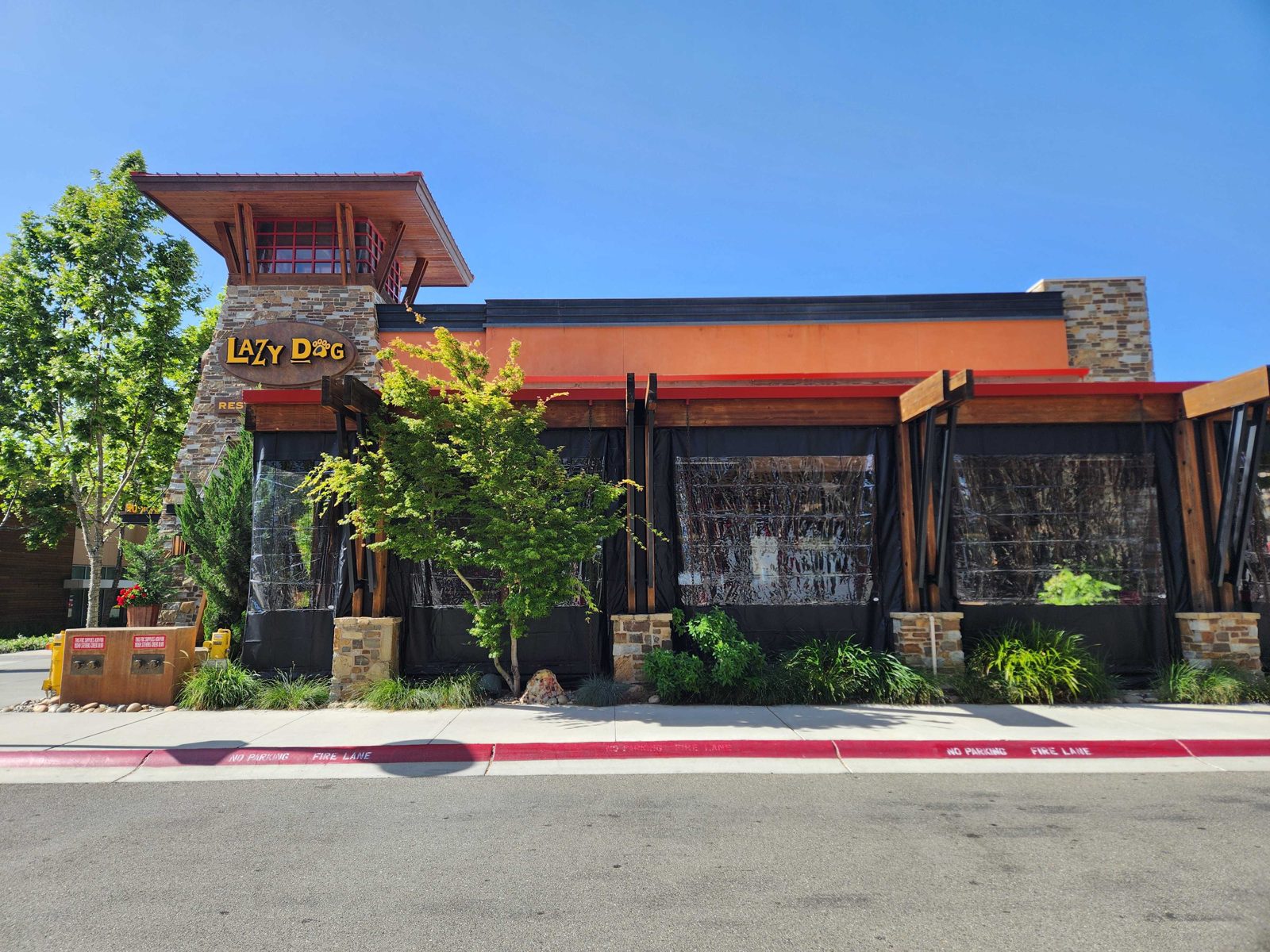 Lazy Dog Cupertino: black-bordered clear panels down along the timber patio under the tower sign, sun shades on the west bays