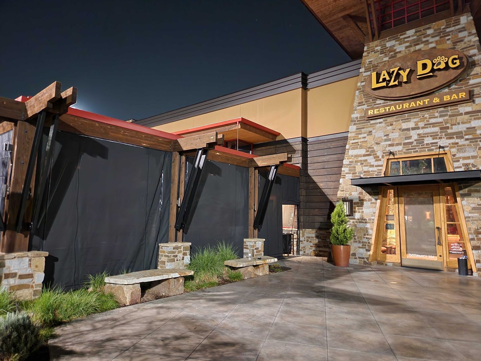 Lazy Dog Downey, California at night: black panels down across the patio beside the lodge entry