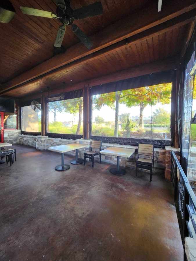 Inside Lazy Dog Folsom, California: the clear panels down along the stone knee wall, the fall trees through the vinyl