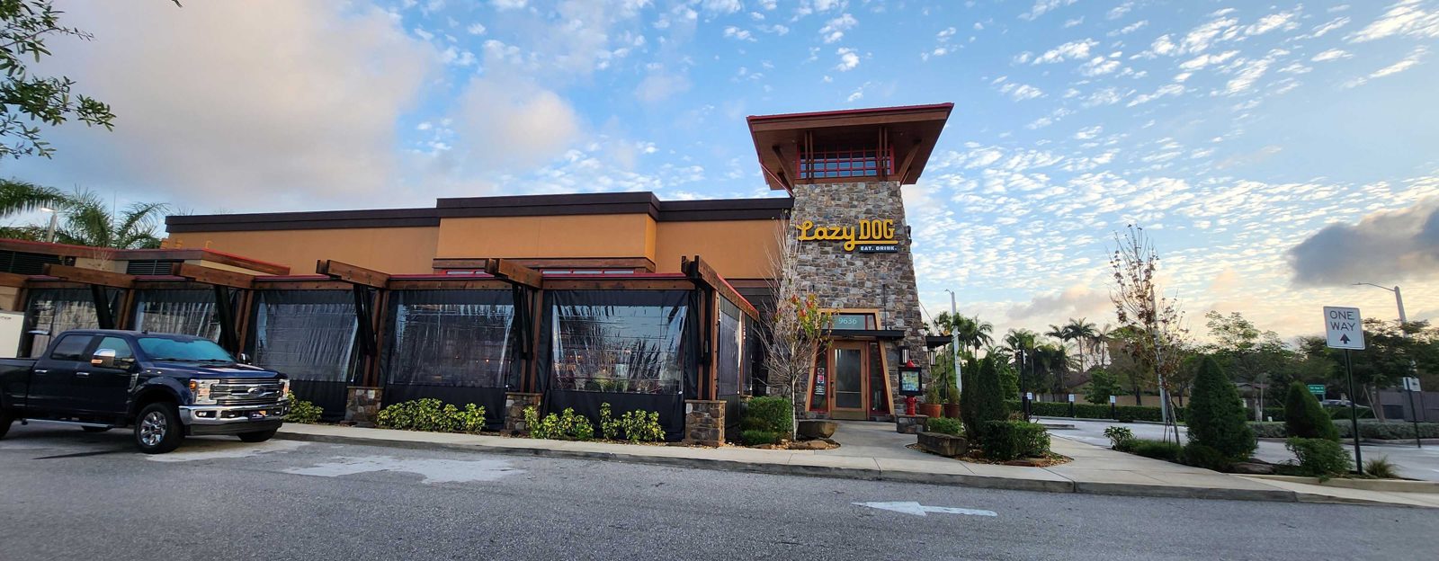 Lazy Dog Boca Raton from the street: clear panels across the timber bays, the stone tower and the sign