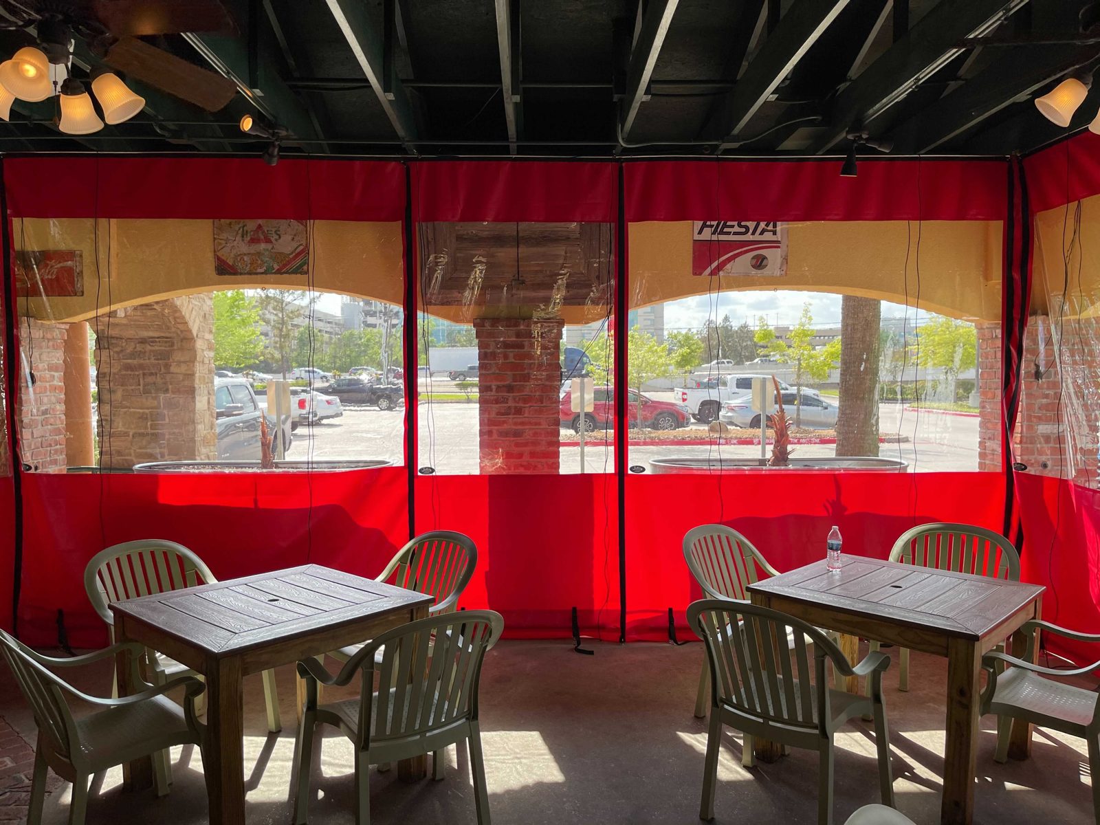 Lupe Tortilla The Woodlands: red-bordered clear panels down around the patio, the stone wall and red umbrellas through the vinyl