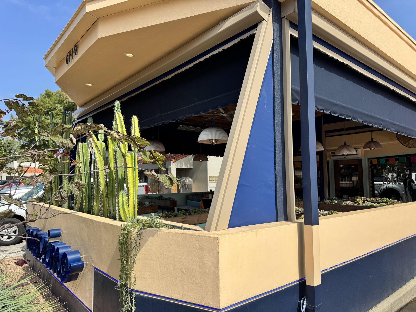 The corner of the patio: a navy triangular return panel between the Sierra Tan post and the awning, cactus in the planter