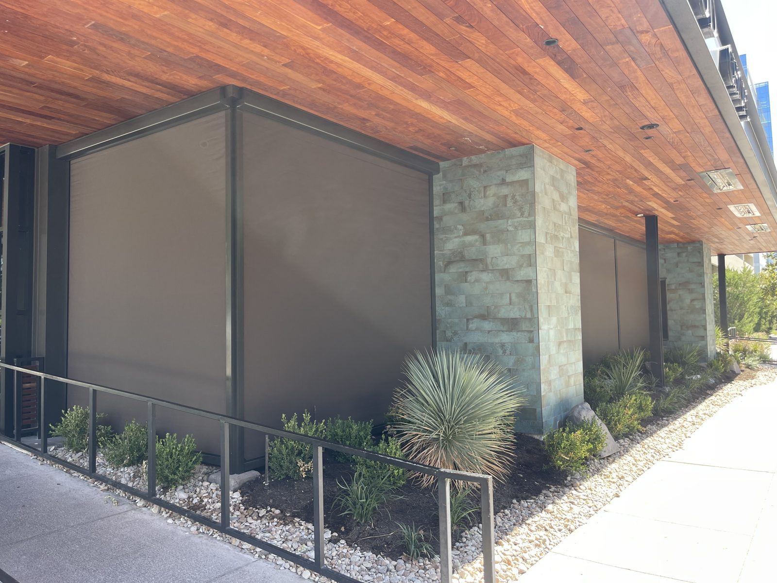 Perry's Austin at The Domain: two tobacco shades meeting at the corner under the wood ceiling, bronze track against the green stone