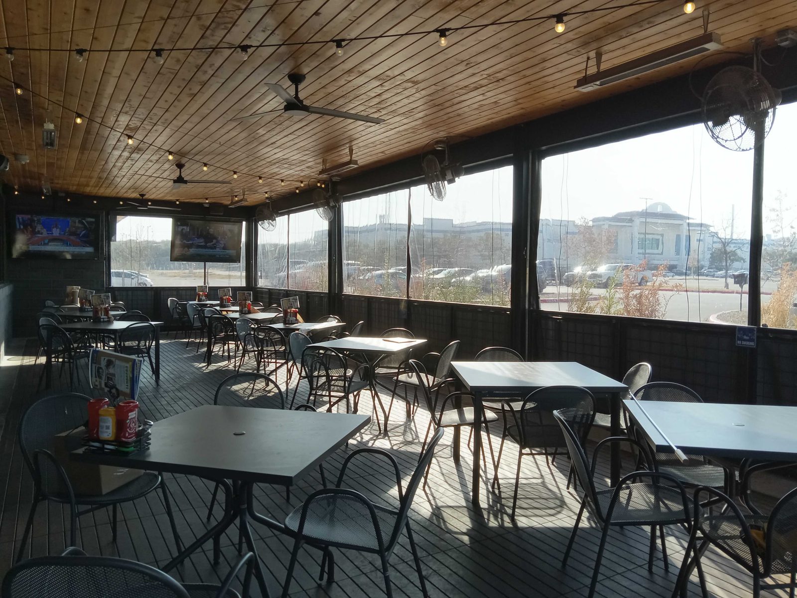 Inside Pluckers Alamo Ranch: the wood ceiling, fans and heaters, the clear panels closed along the rail with the parking lot beyond