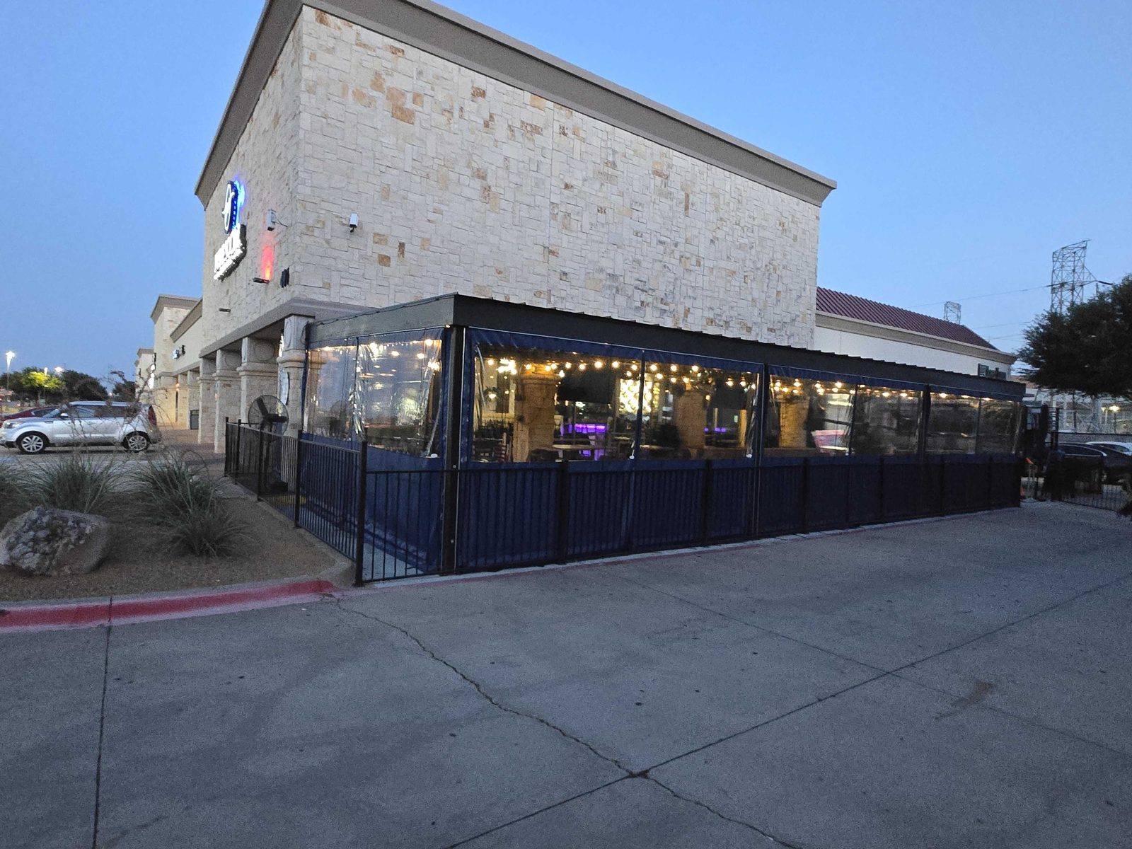 Pure Social in Richardson at dusk: navy and clear panels around the patio, string lights glowing through the vinyl