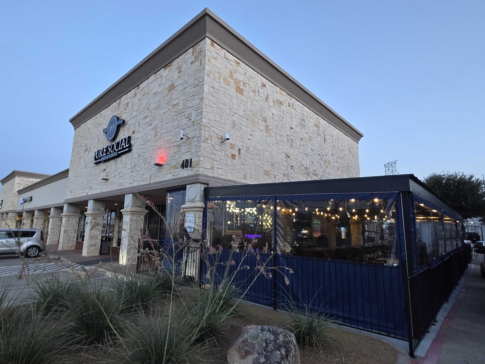 The Pure Social storefront at dusk with the navy and clear panels wrapping the corner of the patio