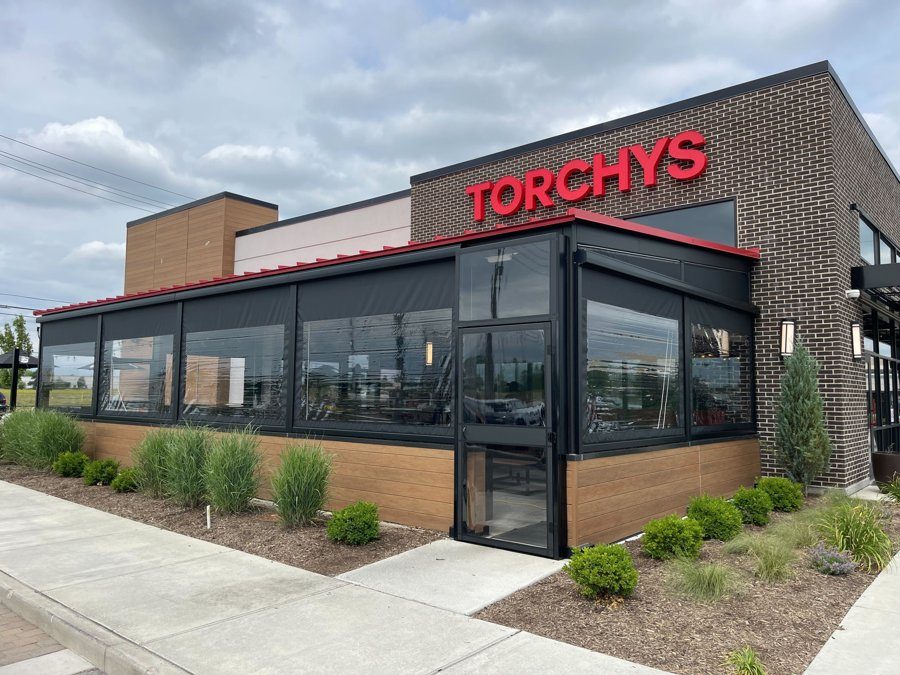 Torchy's Tacos Fishers, Indiana: black motorized screens with clear windows along the brick patio, the framed door at the corner