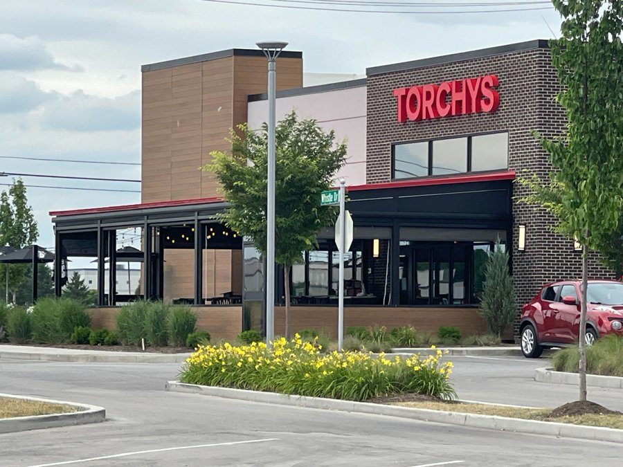 Torchy's Fishers from across the lot: the brick building with the black screens closing the patio under the red eave