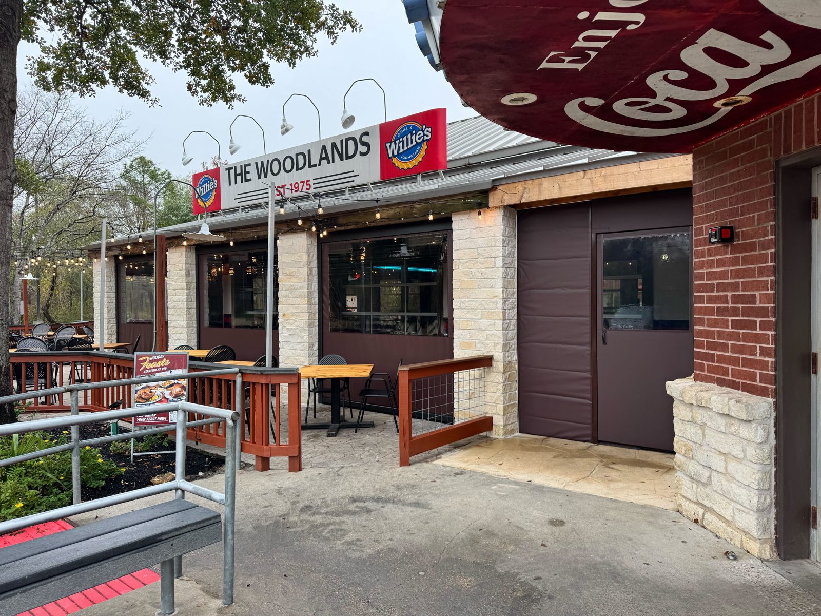 Willie's The Woodlands: brown motorized curtains with clear windows along the porch, the framed door at the brick corner