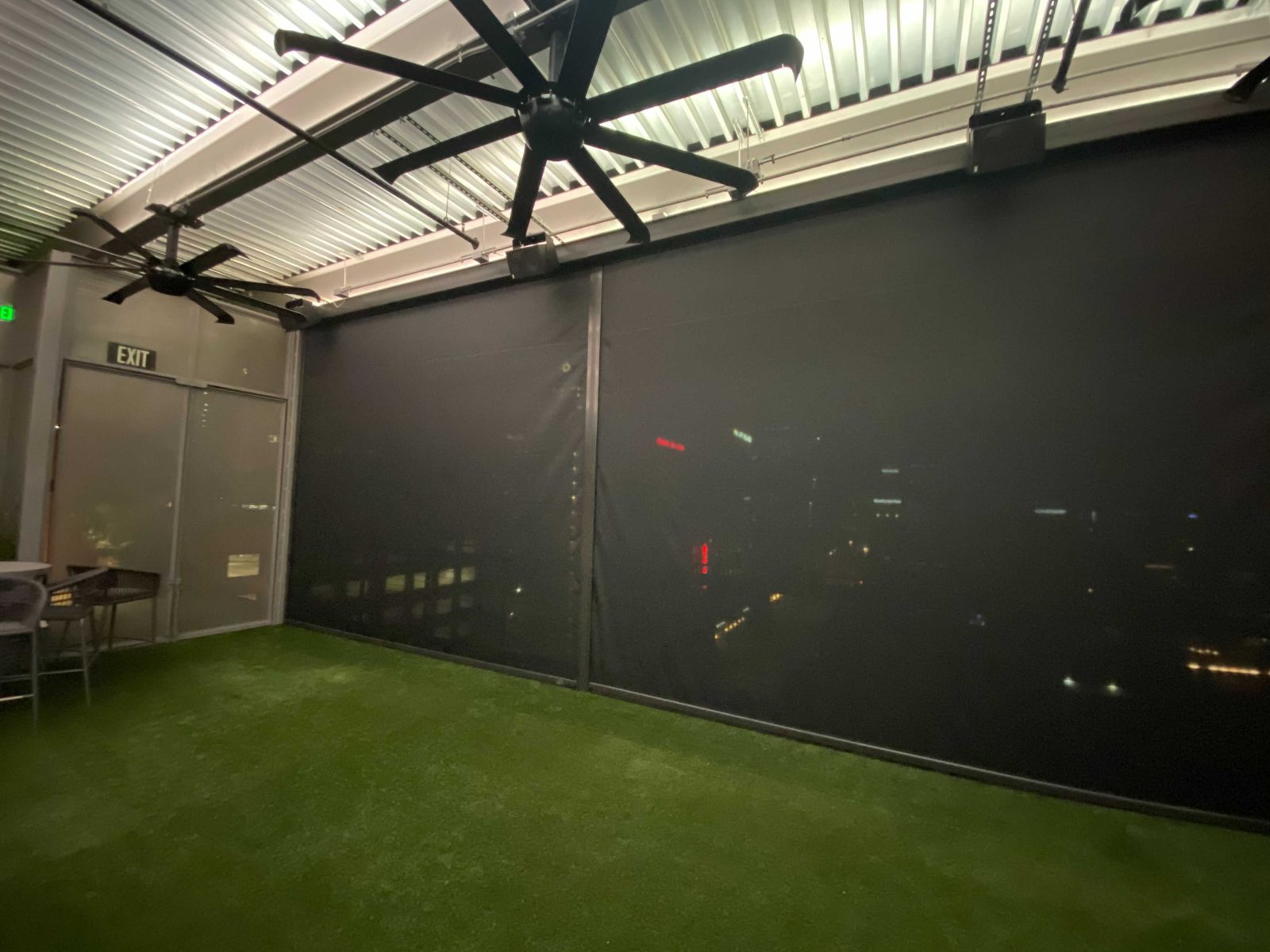 Two black mesh screens down beside the rooftop exit, the fans turning above the turf