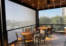 Carve American Grille Austin – Interior View of Motorized Sun Shades & Bug Screens Interior view of motorized sun shades and Nano 50 black bug screens at Carve American Grille in Austin, Texas by Southern Patio Enclosures – showing hoods, side tracks, weight bar, tables, chairs, ceiling fan, and heaters