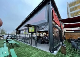 Kirby Ice House Gessner Houston – Manual Clear Vinyl Patio Enclosure Manual roll clear vinyl patio enclosure with black trim at Kirby Ice House Gessner in Houston, Texas by Southern Patio Enclosures – massive panels over 12 ft high on I-beam structure, multiple zipper doors, 15" top and bottom borders, installed with man-lifts for this challenging commercial project