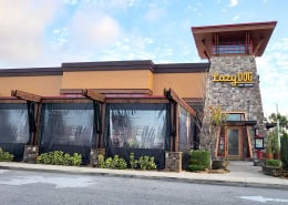 Lazy Dog Restaurant & Bar Boca Raton – Manual Clear Vinyl Patio Enclosure Manual roll clear vinyl patio enclosure with black trim at Lazy Dog Restaurant & Bar in Boca Raton, Florida by Southern Patio Enclosures – 5 panels on the front with custom cutouts around beams and rock base columns for this complex lodge-style restaurant patio