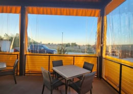 Neighborhood Jam – Interior View of Yellow Border Clear Vinyl Patio Enclosure Interior view looking out through yellow border clear vinyl patio enclosure at Neighborhood Jam by Southern Patio Enclosures – showing ropes, pulleys, zippers, and tie-down systems on the manual roll-down curtains with bright yellow solid vinyl borders