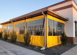 Neighborhood Jam – Yellow Border Clear Vinyl Patio Enclosure Bright yellow border clear vinyl patio enclosure at Neighborhood Jam restaurant by Southern Patio Enclosures – vibrant yellow solid vinyl top and bottom panels with crystal-clear center sections mounted under the awning on a brick storefront