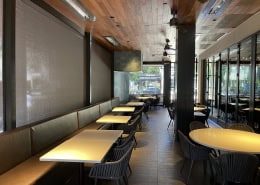 Perry’s Steakhouse & Grille Austin – Interior View of Motorized Nano 97 Tobacco Sun Shades Interior view of motorized Nano 97 Tobacco sun shades at Perry’s Steakhouse & Grille in Austin, Texas by Southern Patio Enclosures – showing upscale dining booths, tables, woven chairs, ceiling fans, and the clean, filtered light coming through the premium motorized shades