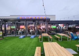 Pluckers Wing Bar Austin (The Linc) – Manual Clear Vinyl Patio Enclosure Manual clear vinyl roll-down patio enclosure at Pluckers Wing Bar The Linc in Austin, Texas by Southern Patio Enclosures – full clear panels with string lights, turf patio, picnic tables, cornhole, and outdoor TVs creating the ultimate sports-bar patio experience